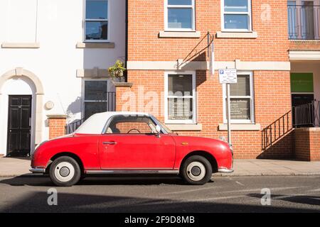 Seitenansicht eines roten Nissan Figaro Cabriolets geparkt An einer sonnigen Vorstadtstraße Stockfoto