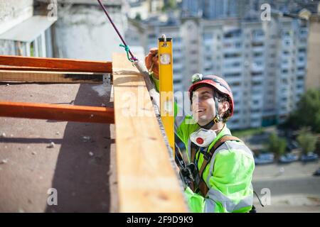 Fröhlicher Industriekletterer, der während der Bauarbeiten mit einem Füllrohr misst Stockfoto