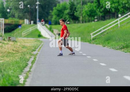 Schöner junger Mann, der sich vor dem morgendlichen Training im Park dehnt und sich aufwärmt Stockfoto
