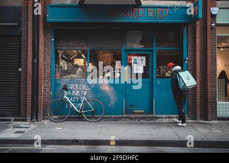 Soho, London - 2021.04.16: Deliveroo Mann Fahrer mit einem Fahrrad wartet auf neue Bestellung. Lieferservice Stockfoto