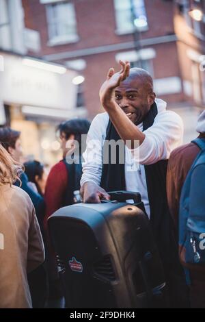 Soho, London - 2021.04.16: Ein Mann mit einem großen Lautsprecher, der durch die Menschenmenge in soho läuft Stockfoto