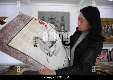 (210418) -- TIANSHUI, 18. April 2021 (Xinhua) -- Huang Jingrong blickt auf einen Seidenteppich im Ausstellungsraum der Seidenteppichfirma Xintian in der Stadt Tianshui, nordwestlich der chinesischen Provinz Gansu, 12. April 2021. Die Stadt Tianshui in der nordwestlichen Provinz Gansu hat eine lange Tradition bei der Herstellung von Seidenteppichen. Die Technik, die mehr als 20 Verfahren umfasst, wurde 2014 aufgrund ihres künstlerischen Wertes und ihrer Komplexität als nationales immaterielles Kulturerbe aufgeführt. Huang Jingrong, 49, begann im Alter von 18 Jahren ihre Reise zur Herstellung von Seidenteppichen in der Xintian Silk Carpet Company. Seit der ersten da Stockfoto