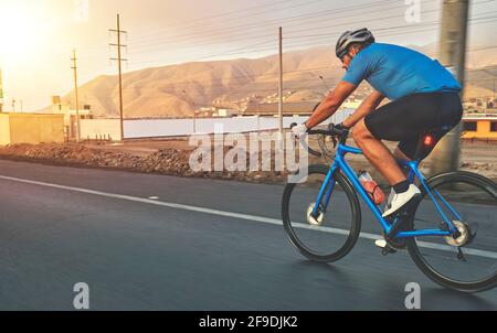 Radsportler, der auf dem Highway bei Sonnenuntergang mit dem Rennrad unterwegs ist. Stockfoto