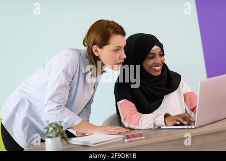 eine afromuslimische Frau mit einem Hijab sitzt lächelnd in ihr Heimbüro und Verwendung eines Laptops für Online-Meetings Stockfoto