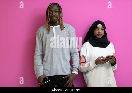 Junges afroamerikanisches Paar lacht mit Smartphones Anwendungen isoliert auf Rosafarbener Studiohintergrund Stockfoto