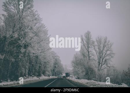 Eine schöne verschneite Autobahn durch den Wald mit wenigen Autos In die gleiche Richtung gehen Stockfoto