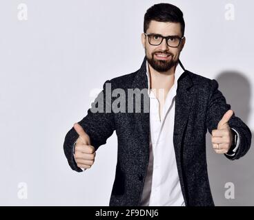 Freundlich lächelnder, stilvoller bärtiger Mann mit Brille und lässigem Tweed Die Jacke steht mit beiden Händen nach oben gestikuliert Stockfoto