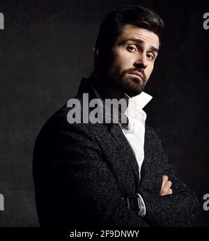 Der junge bärtige Mann in einer stylischen Tweed-Jacke steht neben ihm Kamera mit gekreuzten Armen, die ungläubig auf uns blicken Stockfoto