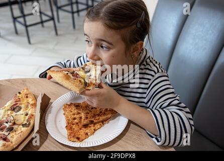 Lustige kleine Mädchen essen Pizza in einem Karton für das Mittagessen. Stockfoto