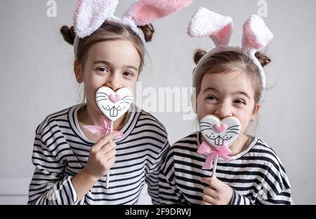 Zwei lustige kleine Schwestern posieren mit OsterLebkuchen in Form von Hasengesichtern. Stockfoto