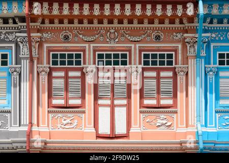 Farbenfrohe Fassade des Peranakan-Einkaufshauses mit Pfirsichfassade und braunen und weißen antiken Holzfensterläden im Morgenlicht im historischen Kotong, Singapur Stockfoto