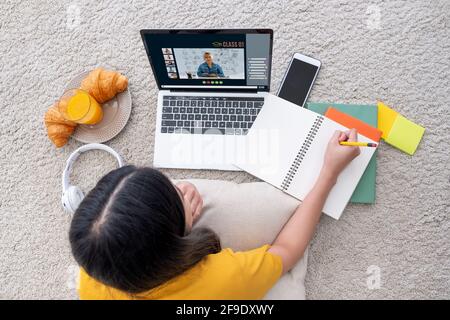 Asiatische weibliche Schüler Videokonferenz mit Lehrer und Freunde mit E-Learning-App auf Laptop-Computer zu Hause.Frau auf Teppich liegend.New normal le Stockfoto