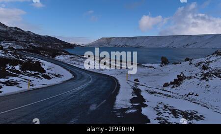 Schöne Aussicht auf kurvenreiche asphaltierte Landstraße am Ufer des Kleifarvatn-Sees in Krýsuvík, Halbinsel Reykjanes, Island, umgeben von Bergen. Stockfoto