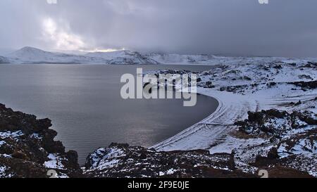 Atemberaubender Blick über den felsigen, schneebedeckten Strand am Ufer des Kleifarvatn-Sees in Krýsuvík, Halbinsel Reykjanes, Island in der Wintersaison mit Bergen. Stockfoto