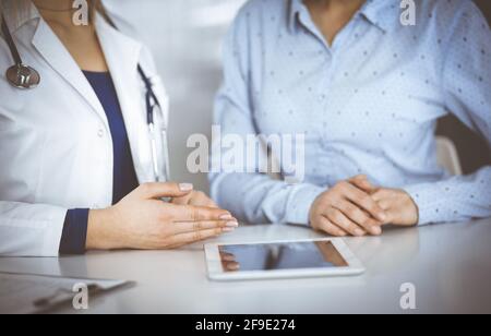 Unbekannte Ärztin zeigt ihrem Patienten eine Beschreibung der Medikation, während sie zusammen am Schreibtisch im Schrank in einer Klinik sitzt. Weiblich Stockfoto