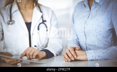 Unbekannte Ärztin zeigt ihrem Patienten eine Beschreibung der Medikation, während sie zusammen am Schreibtisch im Schrank in einer Klinik sitzt. Weiblich Stockfoto