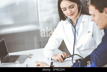 Die junge Ärztin überprüft den Blutdruck ihrer Patientin, während sie zusammen am Schreibtisch in einem Schrank sitzen. Arzt bei der Arbeit in einem Krankenhaus Stockfoto