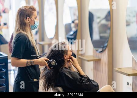 Friseur Trocknen der Haare ihrer Kunden mit einem Haartrockner tragen Schutzmasken in einem Beauty-Center. Stockfoto