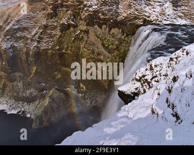 Oberer Teil des berühmten Wasserfalls Skógafoss, ein beliebtes Touristenziel im Süden Islands in der Nähe der Ringstraße, in der Wintersaison mit buntem Regenbogen. Stockfoto