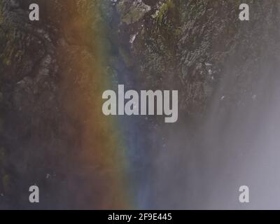 Nahaufnahme des farbenfrohen Regenbogens im Spray des berühmten Skógafoss Wasserfalls mit eisiger Felswand im Hintergrund in der Wintersaison im Süden Islands. Stockfoto