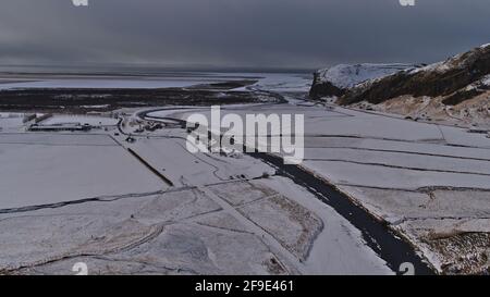 Wunderschöne Luftaufnahme der Südküste Islands mit dem gewundenen Fluss Skógá in der Nähe von Skógafoss und dem Atlantischen Ozean am Horizont am bewölkten Wintertag. Stockfoto