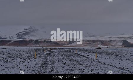 Karge Landschaft mit Wanderweg zum Flugzeugwrack DC-3 in Sólheimasandur an der Südküste Islands mit schneebedeckten Bergen. Stockfoto