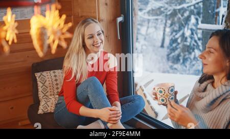Zwei Freundinnen sitzen am Fenster und trinken heiße Schokolade. Winterurlaub. Hochwertige Fotos Stockfoto