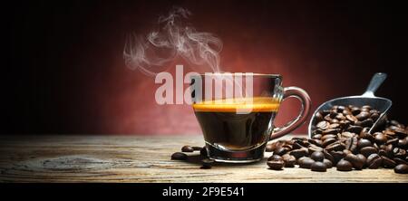 Dampfender Espresso in einer Glastasse mit Kaffeebohnen auf einem alten Holztisch. Platz für Text. Stockfoto