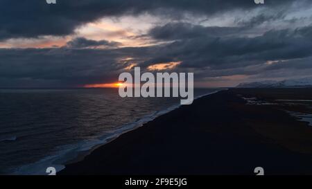 Schöner Sonnenuntergang an der Küste Südislands von der Halbinsel Dyrhólaey aus gesehen, mit langem schwarzen Strand Sólheimasandur und Sonne, die durch Wolken scheint. Stockfoto