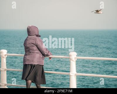 Frau am Meer, die eine Möwe anschaut, die fliegt Über dem Wasser Stockfoto