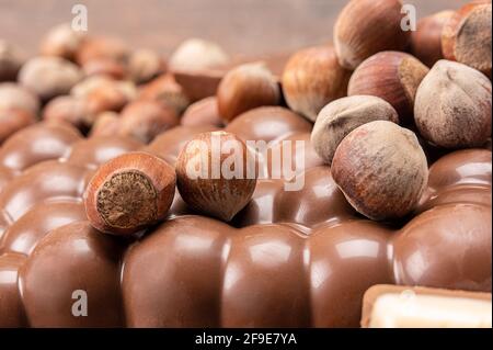 Schokoriegel mit Nüssen. Stapel von Schokoladenstücken mit Haselnüssen auf Holzhintergrund. Verschiedene Sorten Schokolade und Haselnüsse. Haufen gebrochener Chocol Stockfoto