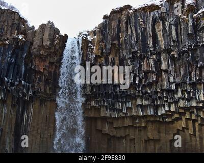 Nahaufnahme der Spitze des atemberaubenden Wasserfalls Svartifoss (schwarze Kaskade) mit bunten sechseckigen Basaltsäulen und Eiszapfen in Skaftafell. Stockfoto