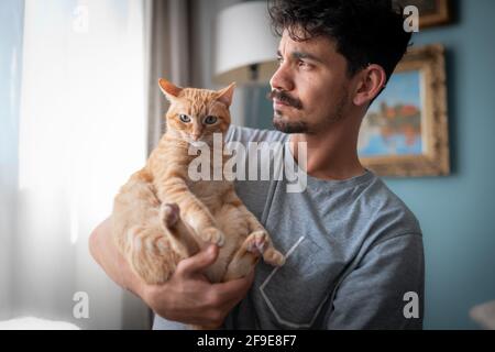 Der junge Mann hält eine braune gestromte Katze in den Armen Stockfoto