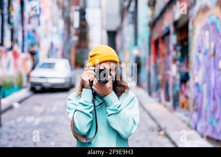 Junger Hipster-Mann in gestricktem Hut, der Graffiti fotografiert Wand auf Kamera in der Stadt Stockfoto