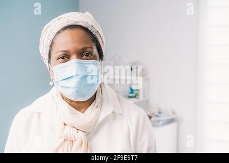 Afroamerikanische reife Patientin mit Gesichtsmaske, die während des Coronavirus-Ausbruchs am Klinikbett auf einen Termin wartet Stockfoto