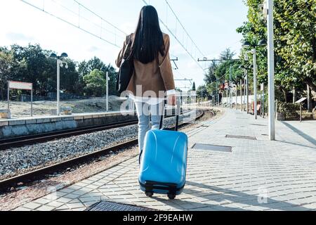 Rückansicht einer anonymen Frau mit Koffer, die entlang ging Bahnsteig am Bahnhof an sonnigen Tagen Stockfoto