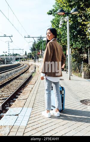 Seitenansicht der asiatischen Reisenden mit Koffer auf dem stand Bahnsteig des Bahnhofs während der Wartezeit auf den Zug Stockfoto