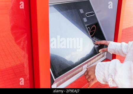 Unbekennbare Frau am Geldautomaten abgeschnitten, während sie Bargeld abheben Steht auf der Stadtstraße Stockfoto