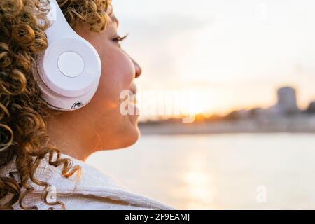 Seitenansicht einer zugeschnittenen, fröhlichen schwarzen Frau in kabellosen Kopfhörern Abends Musik am Strand genießen Stockfoto