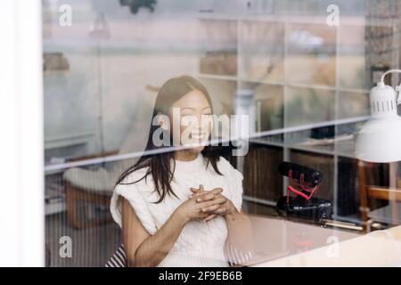 Durch Glasansicht der frohen ethnischen weiblichen Vlogger mit verschlappt Aufnahmen von Videos mit der Kamera im Haus Stockfoto