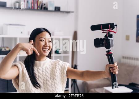 Lächelnde ethnische weibliche Vloggerin, die während der Aufnahme Video auf der Fotokamera aufzeichnete Handgesten im Wohnzimmer Stockfoto