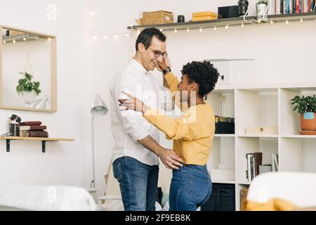 Seitenansicht des entzückten multirassischen Paares, das im Wohnzimmer tanzt Während Sie zu Hause Zeit miteinander verbringen Stockfoto