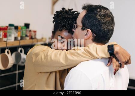 Seitenansicht des liebenden multirassischen Paares, das sich sanft umarmt, während man steht In der Küche zu Hause Stockfoto