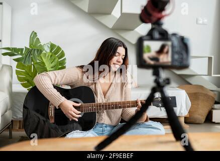 Junge Gitarristin, die akustische Gitarre spielt, während sie ein Video aufzeichnet Fotokamera im Hauszimmer Stockfoto