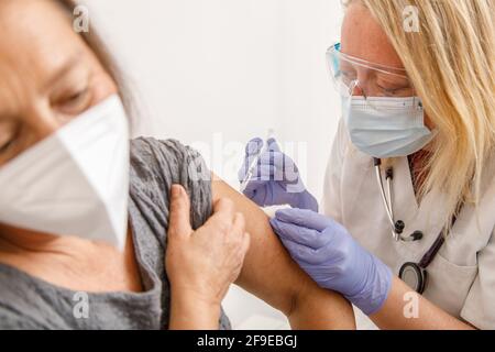 Ärztin für Schutzkleidung und Latexhandschuhe, die impfen Ältere weibliche Patientin in der Klinik während des Coronavirus-Ausbruchs Stockfoto