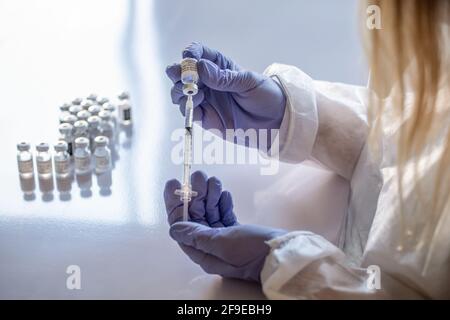 Nicht erkennbarer Sanitäter in schützender Gesichtsschutzmaske und Latexhandschuhen Mit Fläschchen mit Coronavirus-Impfstoff und Spritze, die der Kamera gezeigt wird Im Stehen Stockfoto