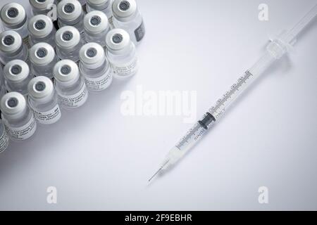 Nahaufnahme einiger Fläschchen mit dem Coronavirus-Impfstoff zusammen mit Eine Nadel auf weißem Hintergrund Stockfoto