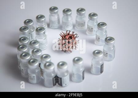 Mikroskopische Simulation des COVID-19-Virusmusters im Hintergrund umgeben von Impfstoffflaschen Stockfoto
