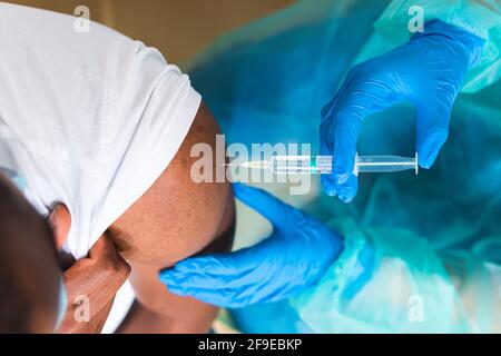 Kurzgeschnittene, nicht erkennbare Ärztin in Schutzkleidung, Latexhandschuhen und Gesichtsmaske zur Impfung afroamerikanischer männlicher Patienten in der Klinik Stockfoto