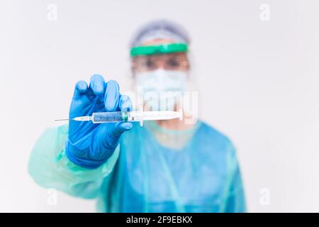 Verschwommener, nicht erkennbarer Sanitäter in schützender Gesichtsschutzmaske und Latex Handschuhe mit Durchstechflasche mit Coronavirus-Impfstoff und Spritze zeigen, bis Kamera während Stan Stockfoto